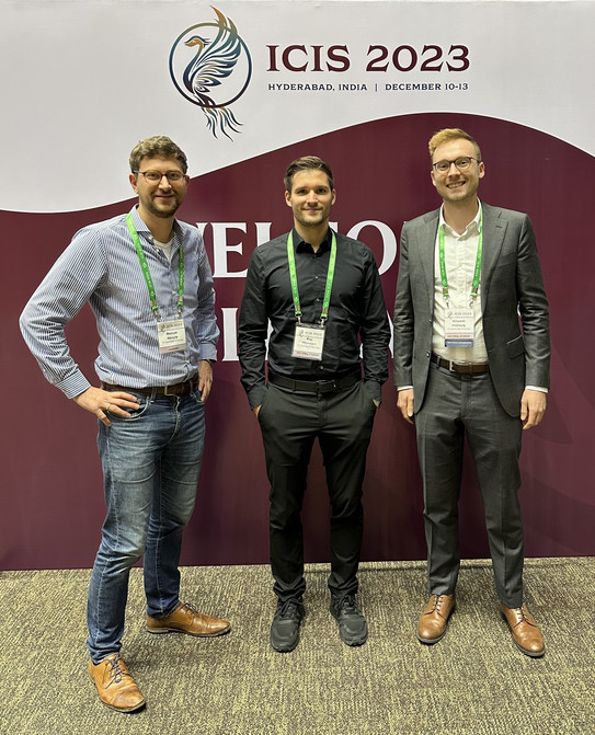 Manuel Wiesche, Kay Hönemann and Vincent Heimburg in front of a logo of ICIS 2023