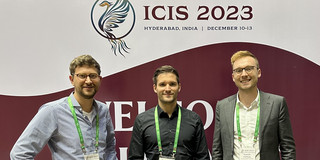 ICIS 2023 Manuel Wiesche, Kay Hönemann and Vincent Heimburg in front of a logo of ICIS 2023