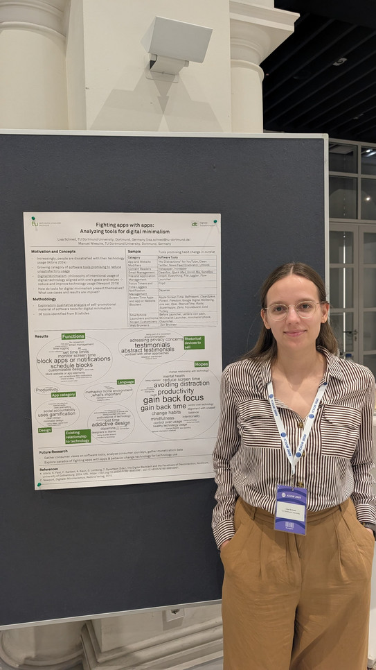 Das Bild zeigt eine vertikale Innenaufnahme einer jungen Frau, die rechts neben einem wissenschaftlichen Poster steht, das an einer dunkelblauen Stellwand befestigt ist. Die Frau hat schulterlanges, braunes Haar und trägt eine runde Brille. Sie lächelt freundlich direkt in die Kamera. Ihre Kleidung besteht aus einer längs gestreiften Bluse in Braun und Weiß sowie einer locker sitzenden, hellbraunen Hose. Ihre Hände hat sie lässig in den Hosentaschen vergraben. Um den Hals trägt sie ein weiß-blaues Schlüsselband (Lanyard) mit der Aufschrift „ICSOB 2024“ und einem daran befestigten Konferenzausweis.